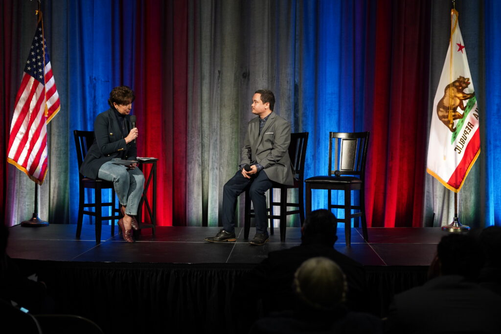 A moderator and political candidate on stage asking and answering questions to a 50 person audience