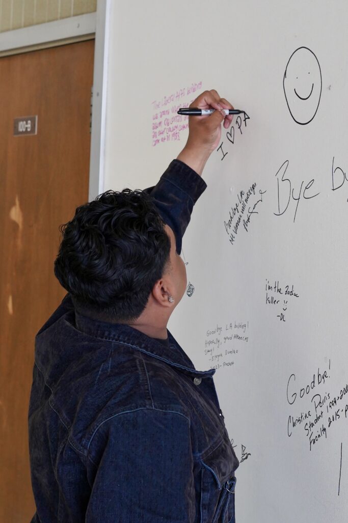 An attendee using a marker to write a note on a wall, thanking the liberal arts building for its service.